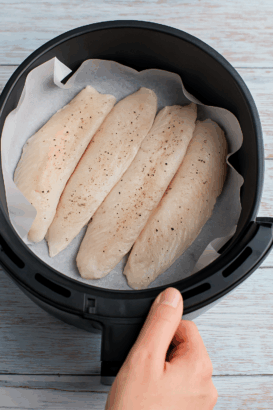 Filés de peixe crus alinhados na cesta da air fryer com papel manteiga