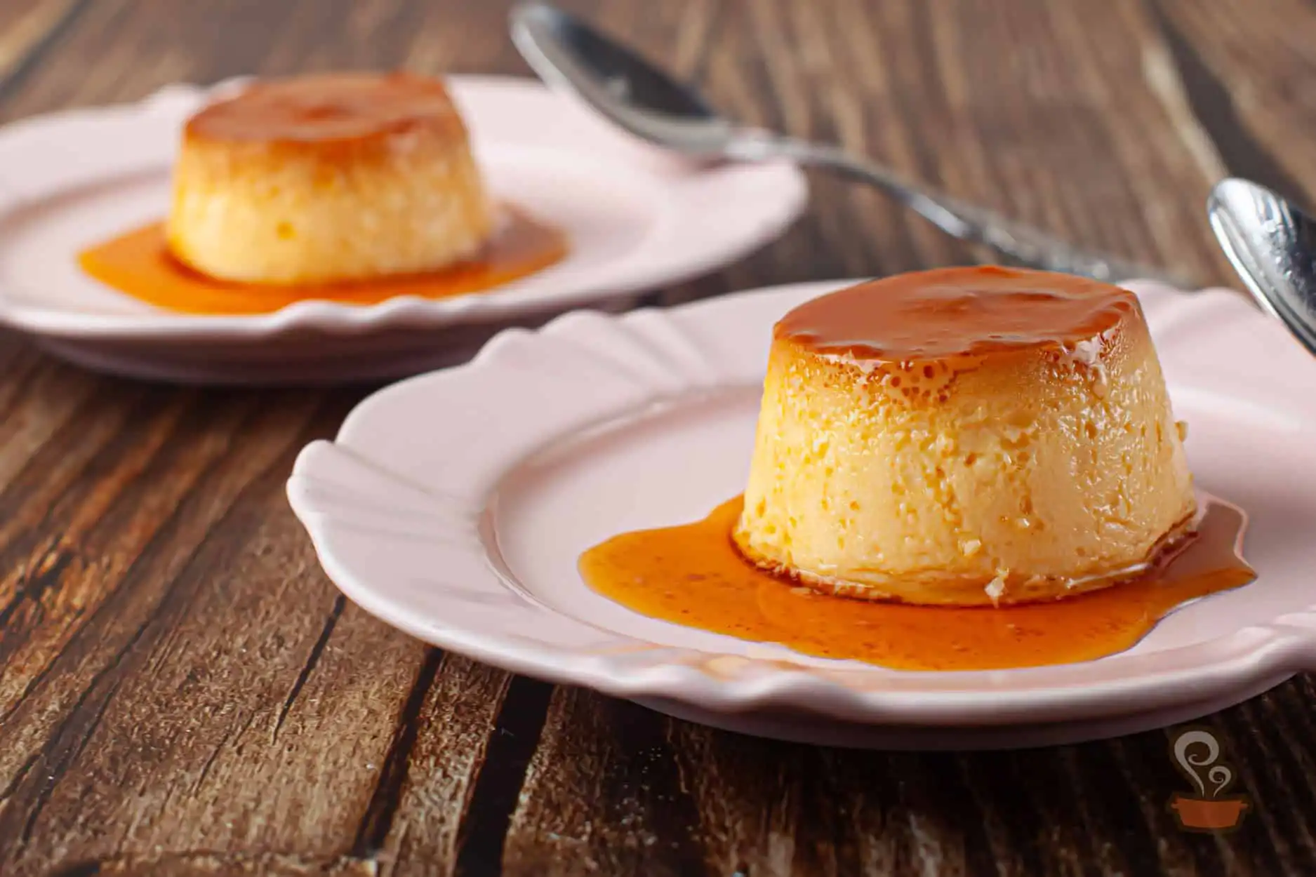 Pudim cremoso com calda escorrendo sobre louça clara com colher ao fundo