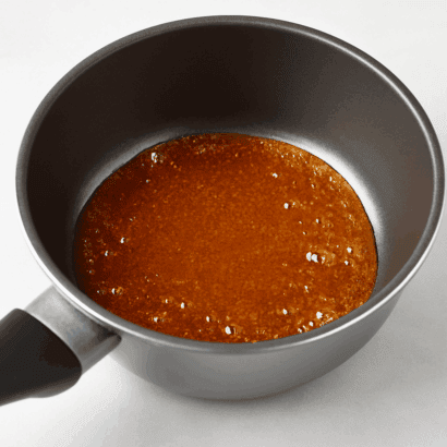 Caramelo dourado borbulhando em panela antiaderente sobre fundo branco