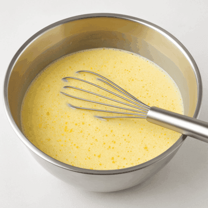 Mistura cremosa de pudim com raspas de laranja em tigela inox com fouet