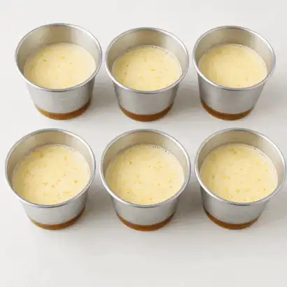 Forminhas de alumínio com creme de pudim cru e base de caramelo sobre fundo claro